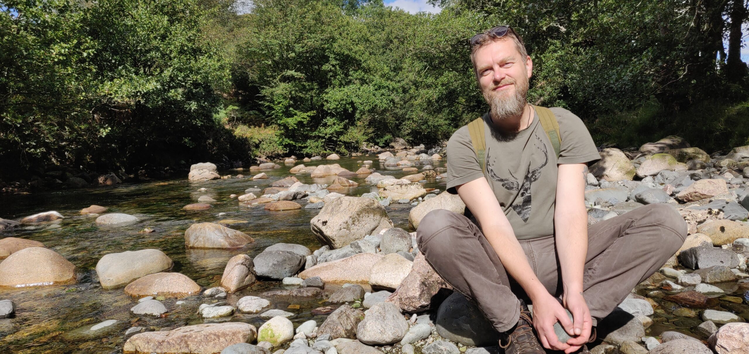 Tony sitting on pebbles next to a river